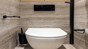 Ein modernes Badezimmer mit Toilette in Weiß, einem schwarzen Bidet und einer Marmorwand.