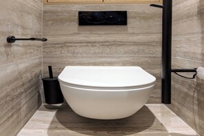 Een moderne badkamer met een wit toilet, een zwart bidet en een marmeren wand.