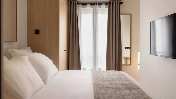 Ein Hotelzimmer mit Bett, Vorhängen, einem an der Wand montierten Fernseher und einem Fenster mit Blick.