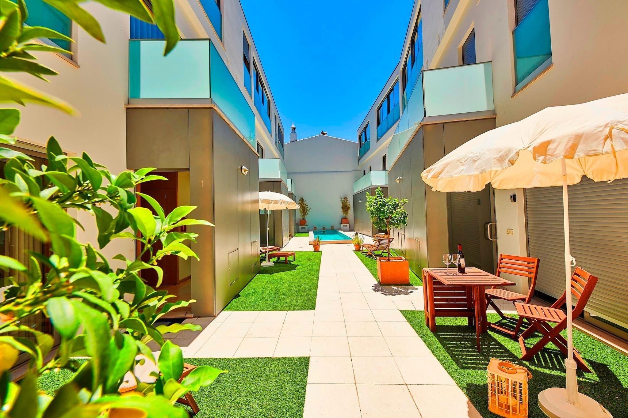 Un patio estrecho con piscina, mobiliario exterior y plantas en macetas.