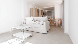 Ein modernes Wohnzimmer mit einem weißen Sofa, einem Metall-Couchtisch und einer Küche im Hintergrund.