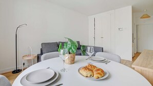 Ruokailutila, jossa on pyöreä pöytä, lautasia, kasvi korissa ja croissant.