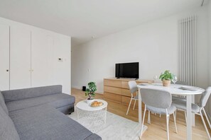 A modern living room with a grey sofa, a round coffee table, a dining table with chairs, a TV, and a small plant. - Charming studio - 2P - balcony - Saint Honore (Paris)