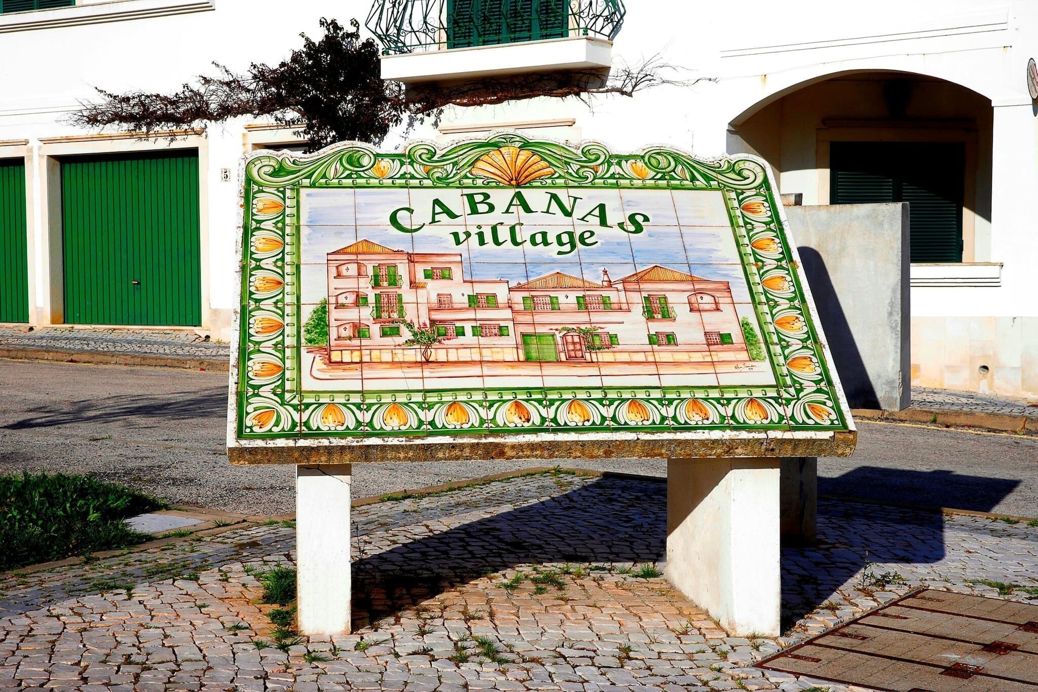 Een bord met 'CABANAS village' en een kleurrijke illustratie van gebouwen.