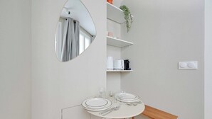 A dining area with a round table set for two, a mirror, and shelves above holding kitchen items. - Cosy Studio 2P - Paris 01/Musée du Louvre (Paris)