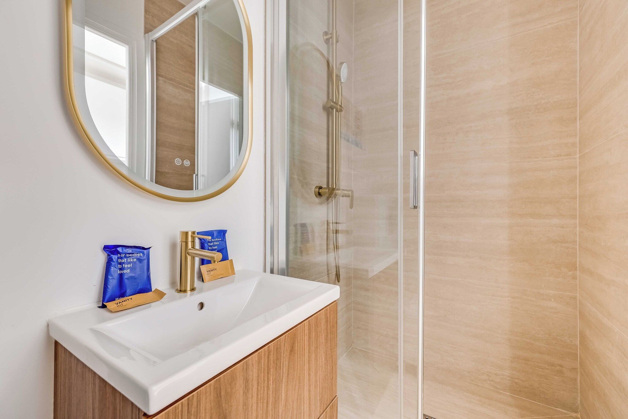 A bathroom with a white sink, a gold faucet, and a glass shower enclosure.
