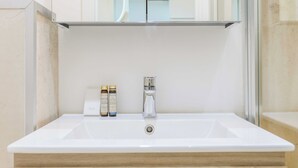 Un tocador de baño con un lavamanos blanco, un espejo encima y dos botellas de champú y gel en la encimera.