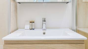 Un tocador de baño con un lavamanos blanco, un espejo encima y dos botellas de champú y gel en la encimera.