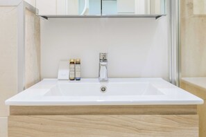 Valkoinen pesuallas, sen yläpuolella peili sekä kaksi pulloa shampoota ja suihkugeeliä ovat kylpyhuoneen tasolla.