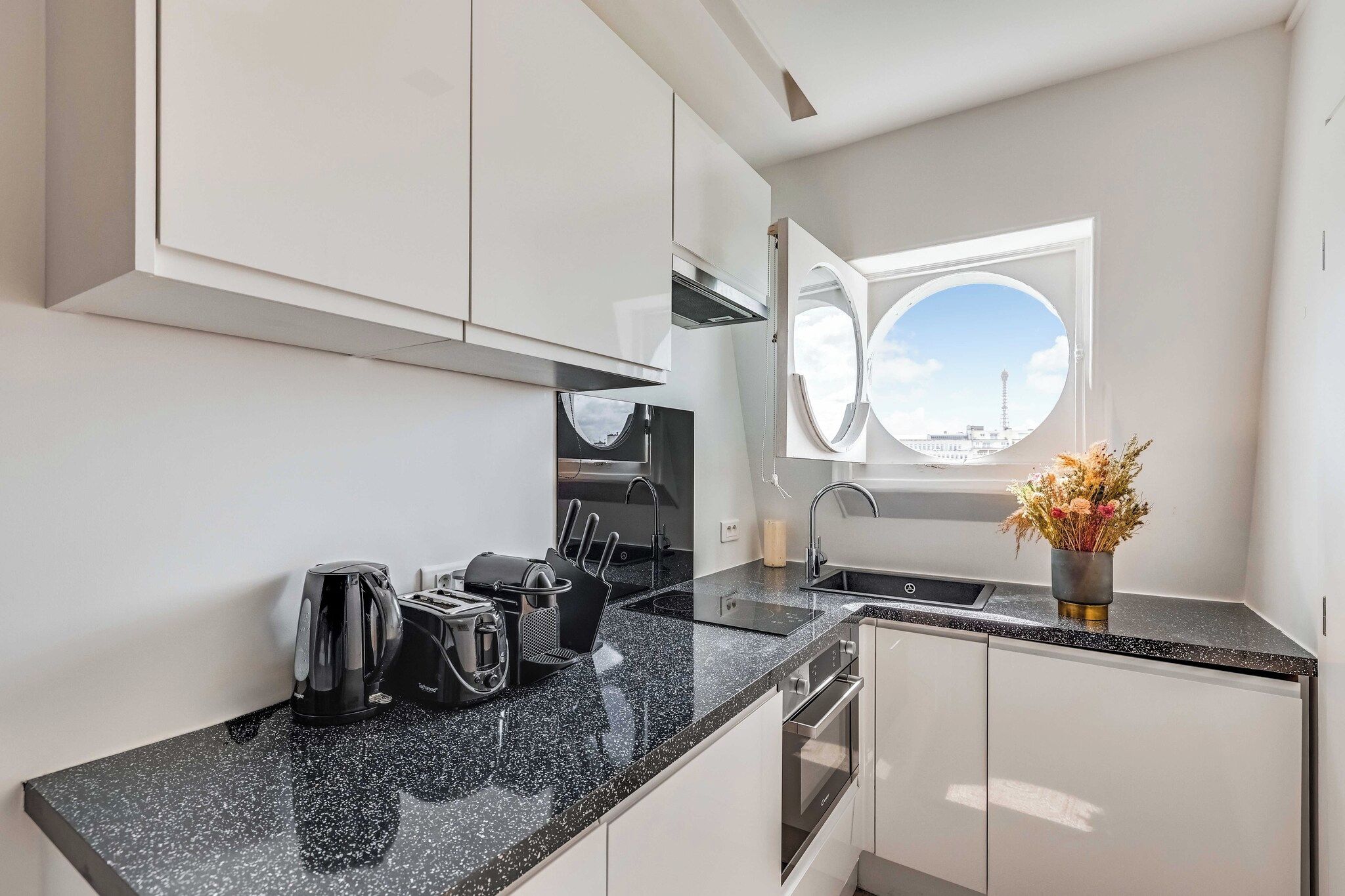 A modern kitchen with a black granite countertop, stainless steel appliances, and a window with a view of a tower.