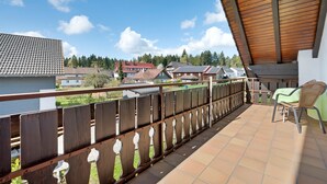 A balcony with a wooden railing, a chair, and a view of houses and trees.