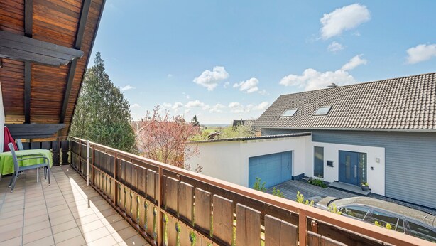 Un balcon doté d’une balustrade en bois, une table avec des chaises et une vue sur une maison moderne avec un garage.