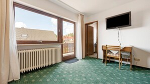 Une pièce dotée d’une grande fenêtre, d’un radiateur, d’un bureau avec une chaise et d’un téléviseur fixé au mur.