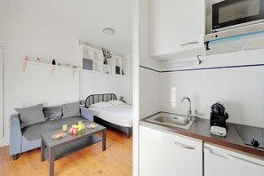 A compact living space with a kitchenette, a bed, a sofa, and a coffee table with breakfast items. - Elegant Studio 2P – Paris 14 (Paris)