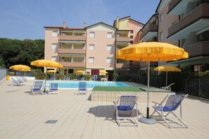 Un espace piscine doté de chaises longues et de parasols jaunes, entouré d’immeubles d’appartements.