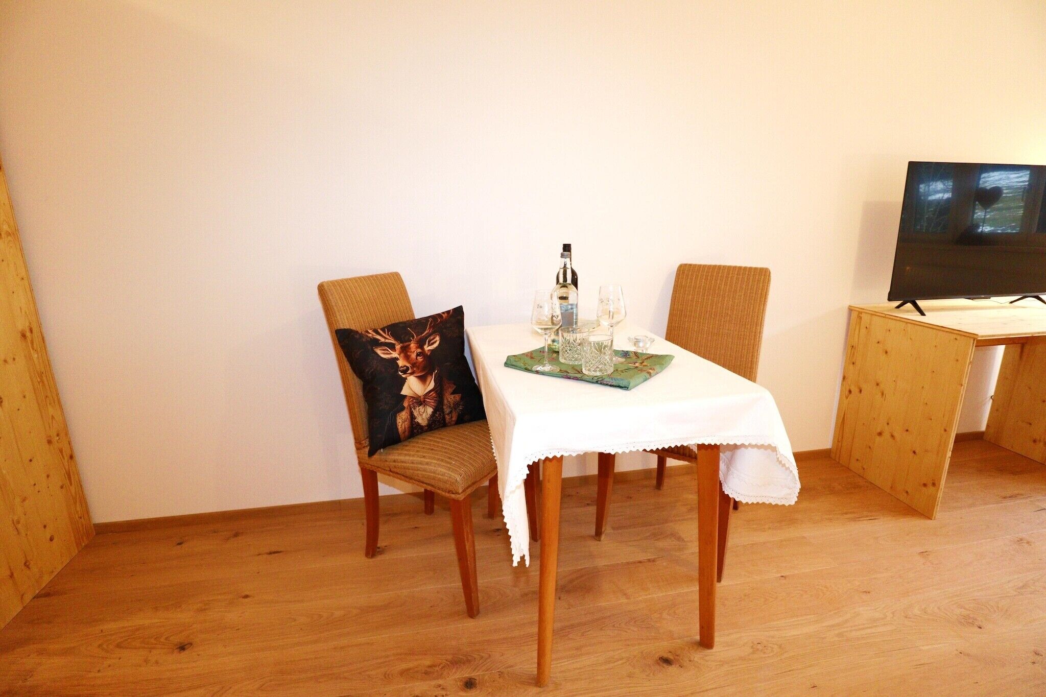 Un comedor con una mesa lista para dos, un televisor sobre un mueble bajo y suelo de madera.