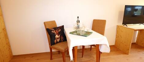 Un comedor con una mesa lista para dos, un televisor sobre un mueble bajo y suelo de madera.