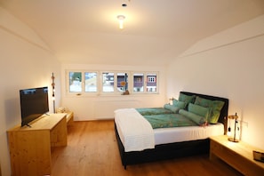 A bedroom with a bed, a TV, a desk, and a window with a view of buildings.