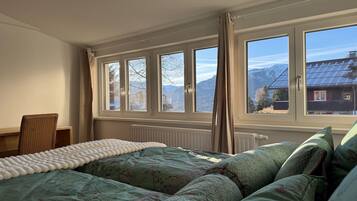 A bedroom with a bed, a chair, and a view of mountains through large windows.