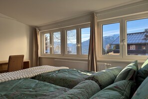 Ein Schlafzimmer mit einem Bett, einem Sessel und Bergblick durch große Fenster.