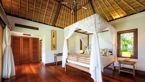 A bedroom with a four-poster bed, wooden flooring, a ceiling fan, and a window with blinds. - Villa Maridadi Cemagi (Cemagi)