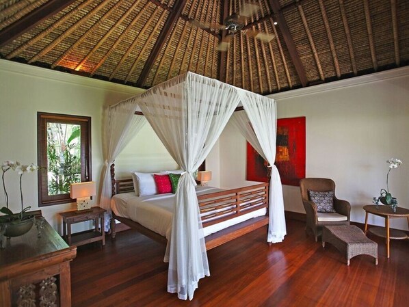 A bedroom with a four-poster bed, a wooden floor, a chair, a small table, and a window with a view of greenery. - Villa Maridadi Cemagi (Cemagi)