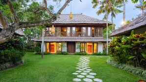 A two-story house with a thatched roof, a stone pathway leading to the entrance, and lush greenery surrounding the property. - Villa Maridadi Cemagi (Cemagi)