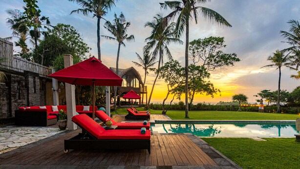 A poolside area with red lounge chairs, a wooden deck, and a view of the sunset. - Villa Maridadi Cemagi (Cemagi)