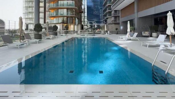 Ein moderner, überdachter Pool mit Liegestühlen und Sonnenschirmen, umgeben von Hochhäusern.