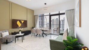 Ein modernes Wohnzimmer mit einer Couch, einem Esstisch mit Stühlen, einem Flachbildfernseher und einem großen Fenster mit Blick auf die Stadt.