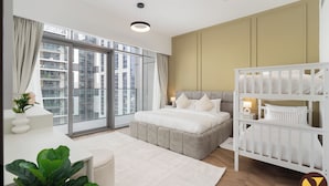 Ein modernes Schlafzimmer mit großem Fenster, einem Bett, einem Reisebett und einem Nachttisch mit Lampe.