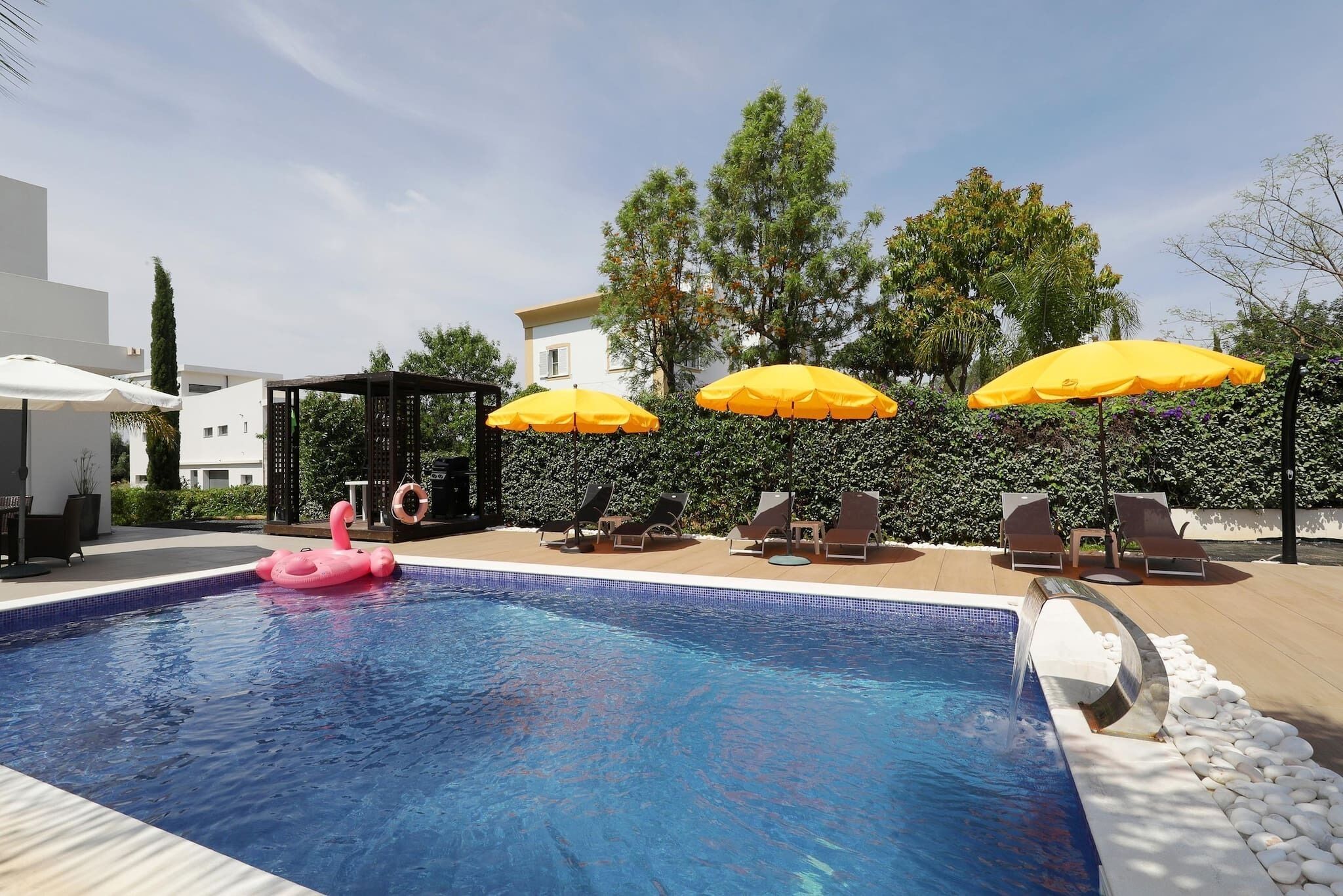 Une piscine avec un flotteur rose, entourée de chaises longues et de parasols jaunes.