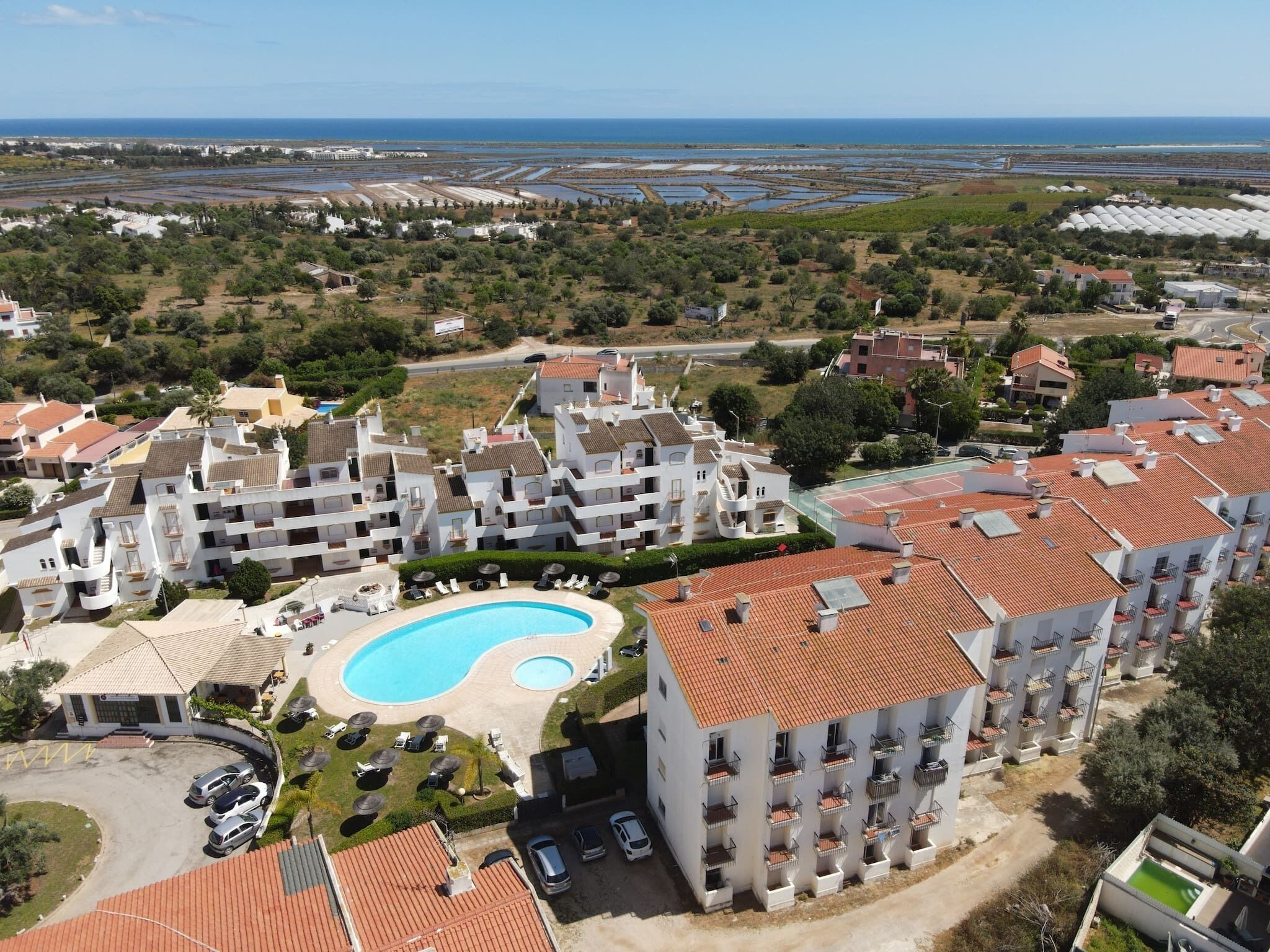 A coastal hotel with multiple buildings, a swimming pool, and a view of the sea.