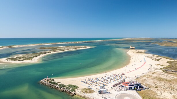 Vista aérea de un complejo turístico en la playa, con una playa de arena, aguas azules cristalinas y un pequeño muelle.