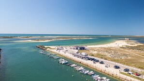 Una marina costera con barcos amarrados, un muelle y una zona de playa con un edificio que dice 'Beach & House'.