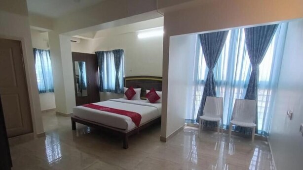 A hotel room with a bed, a bench, two chairs, a mirror, and a door. - Hotel Amulya Relax Inn  (Bengaluru)