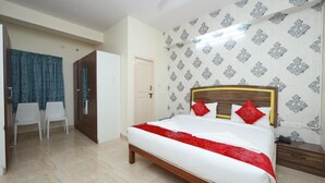 A hotel room with a bed, a wardrobe, a desk, and chairs. - Hotel Amulya Relax Inn  (Bengaluru)