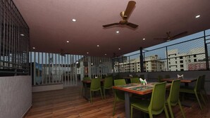 A restaurant with wooden flooring, green chairs, and tables. - Hotel Amulya Relax Inn  (Bengaluru)