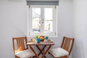 A small dining table with two wooden chairs, a window with a view of the street, and a fruit bowl on the table. - STUDIO LARGO, Town Centre (Tavira)
