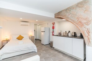 A modern hotel room with a bed, a small kitchenette, and a stone accent wall. - STUDIO LARGO, Town Centre (Tavira)