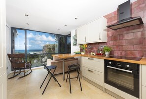 Eine moderne Küche mit Meerblick, eine Essecke mit Tisch und Stühlen sowie ein eingebauter Backofen.