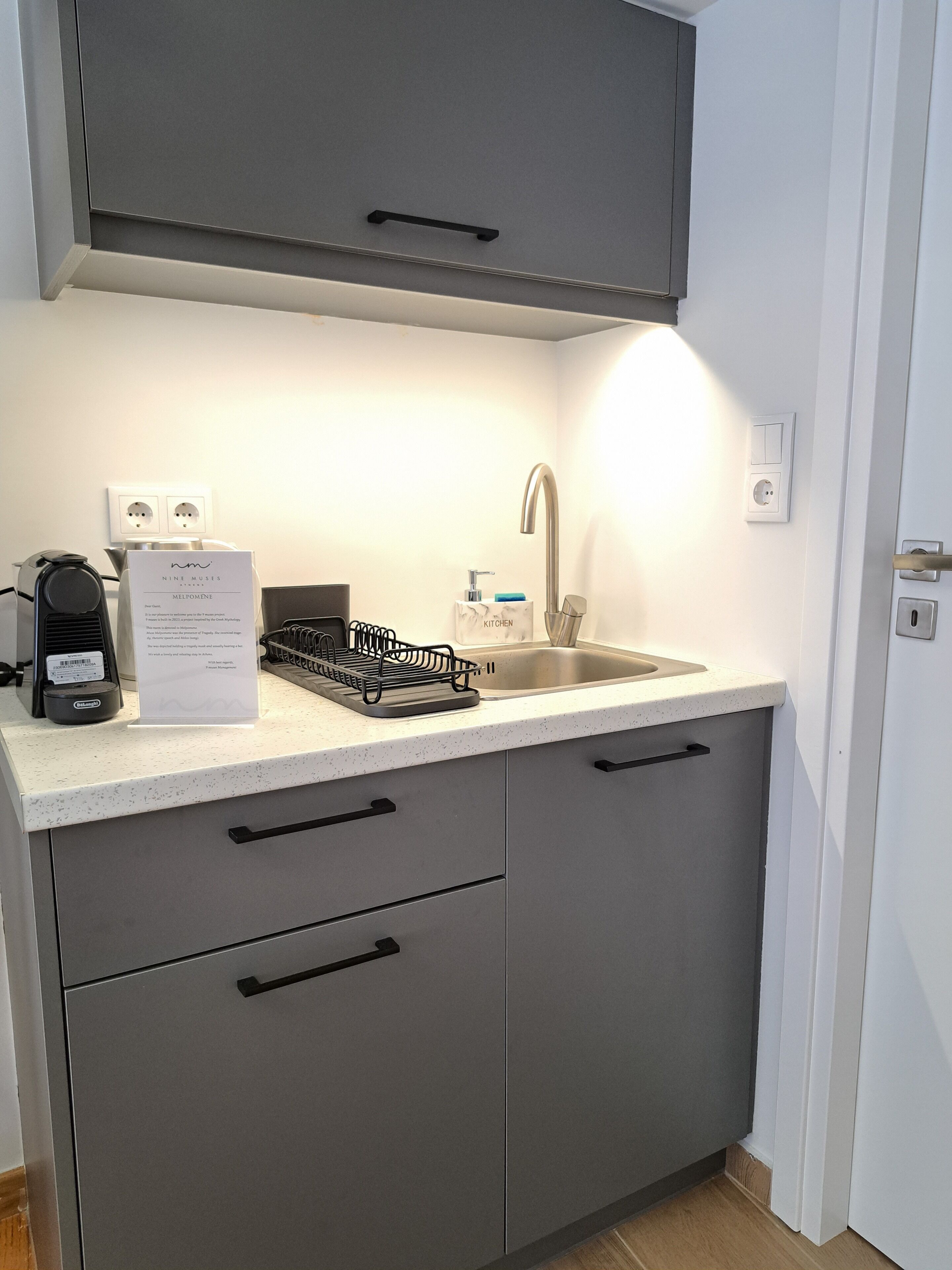 A compact kitchen with a sink, a coffee machine, and a dish rack.