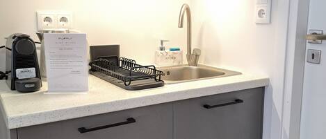 A compact kitchen with a sink, a coffee machine, and a dish rack.