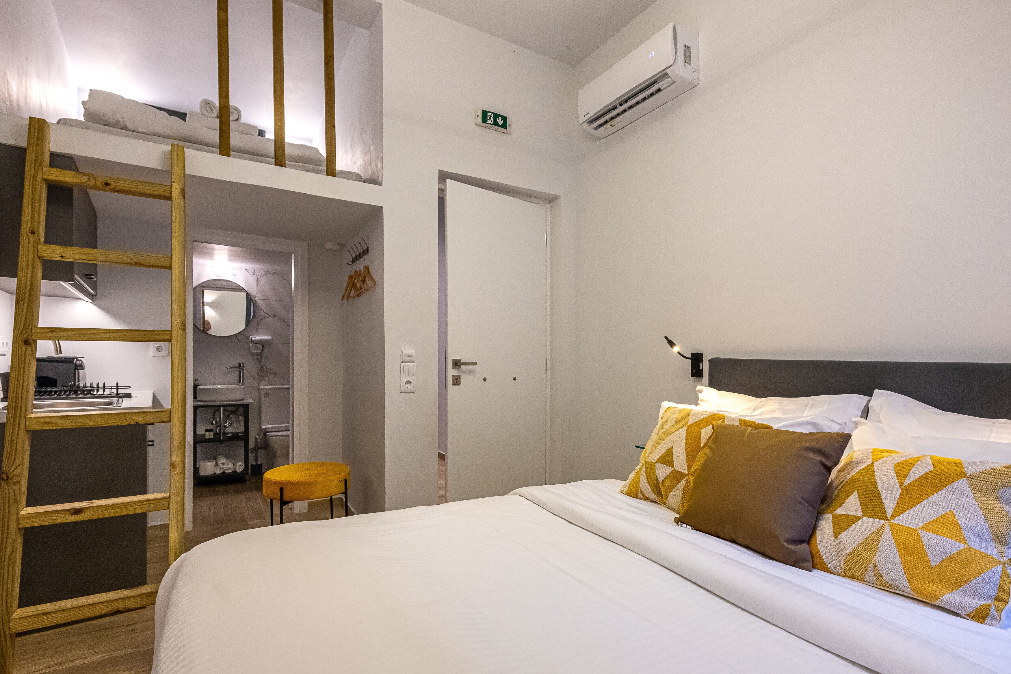 Un dormitorio con literas, una kitchenette pequeña, un baño y una puerta con letrero de salida de emergencia.