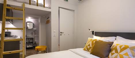 Un dormitorio con literas, una kitchenette pequeña, un baño y una puerta con letrero de salida de emergencia.