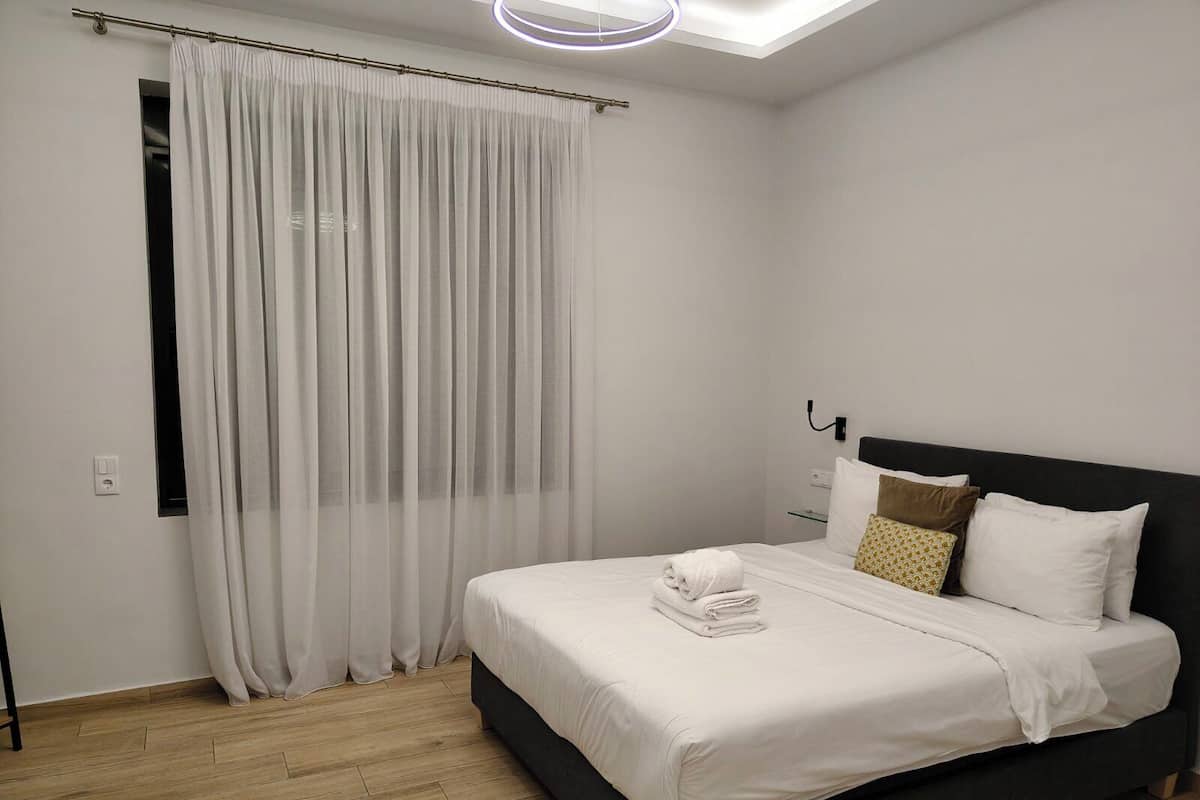 A modern bedroom with a large bed, a window with sheer curtains, and a skylight.