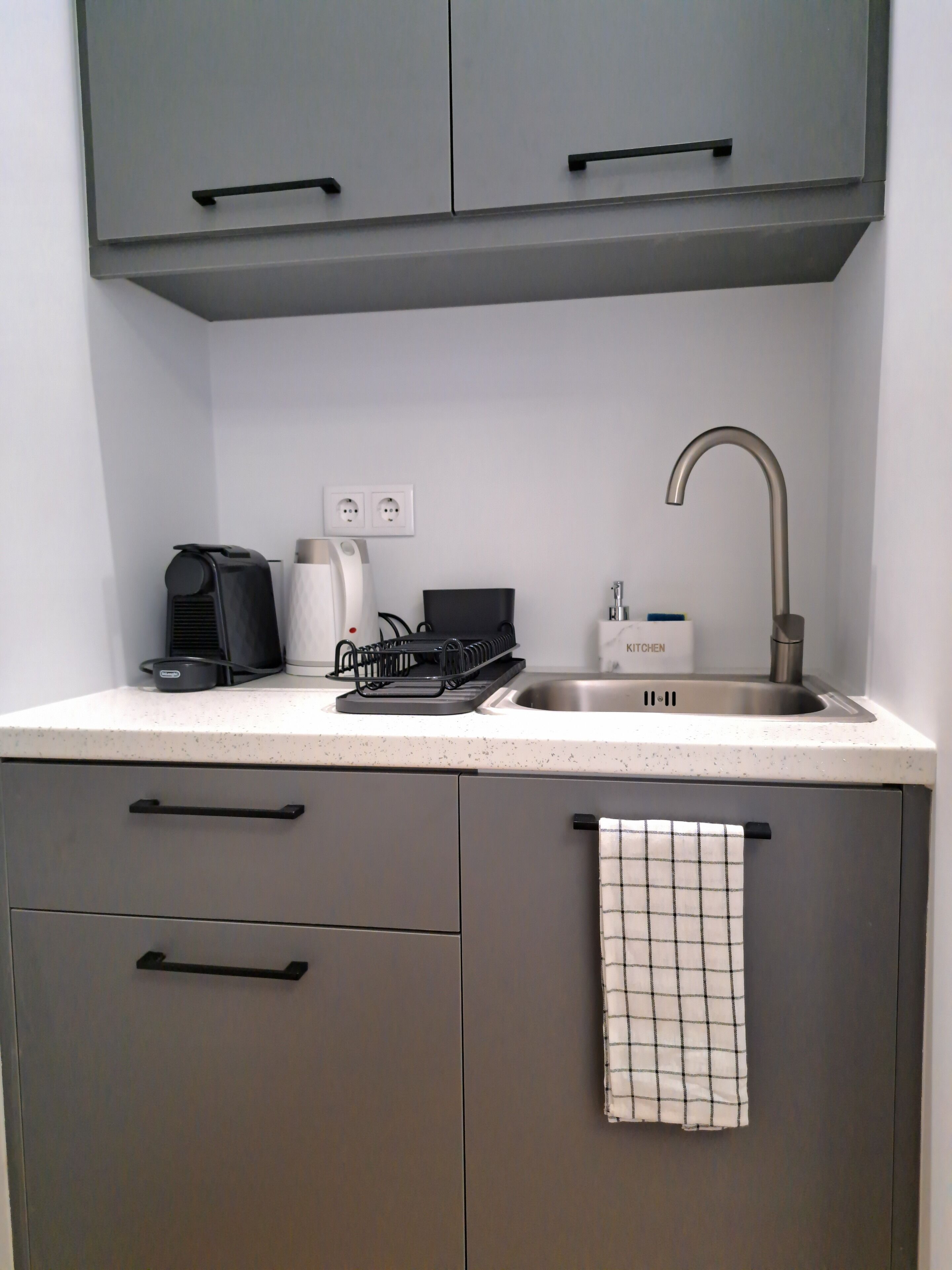 A compact kitchen with a sink, a coffee maker, and a kettle.