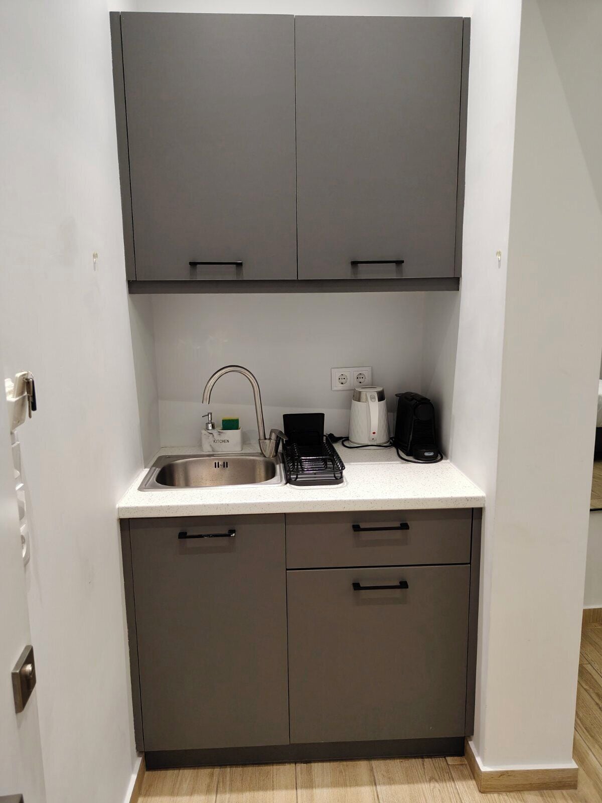 A compact kitchen with grey cabinets, a stainless steel sink, and a coffee maker.