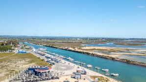 Un port de plaisance situé sur la côte, avec des bateaux amarrés le long du rivage, une plage de sable avec des parasols et des sièges, et une vue dégagée sur le paysage environnant.