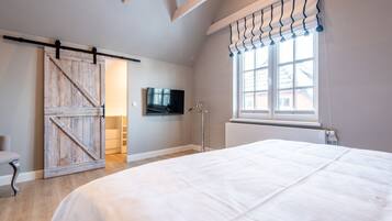 A bedroom with a large bed, a sliding barn door closet, a TV mounted on the wall, and a window with curtains.